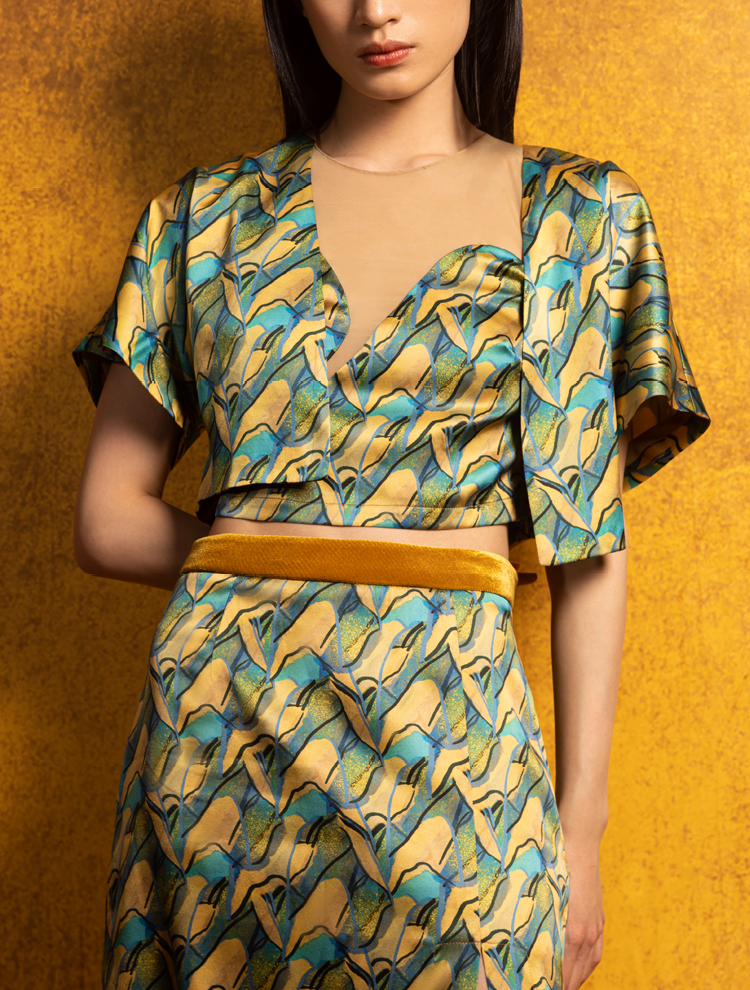 A woman wears a silk crop top, skirt, and jacket. The set features the PANORAMA Print and is inspired by Chinese landscape paintings. She exudes grace in this Modern Chinese chic style.