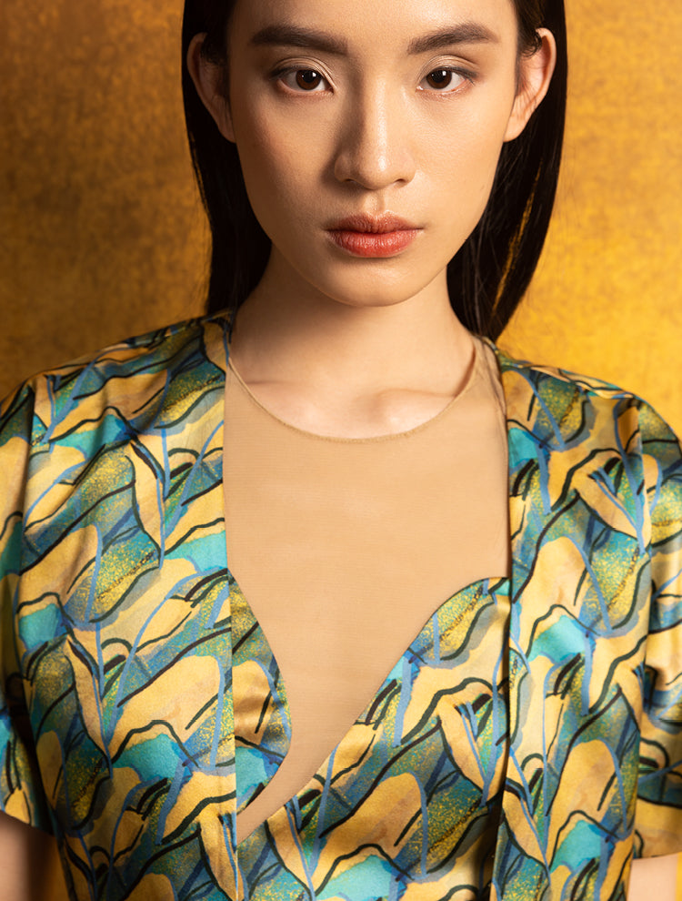 A woman wears a silk crop top and jacket. The set features the PANORAMA Print and is inspired by Chinese landscape paintings. She exudes grace in this Modern Chinese chic style.