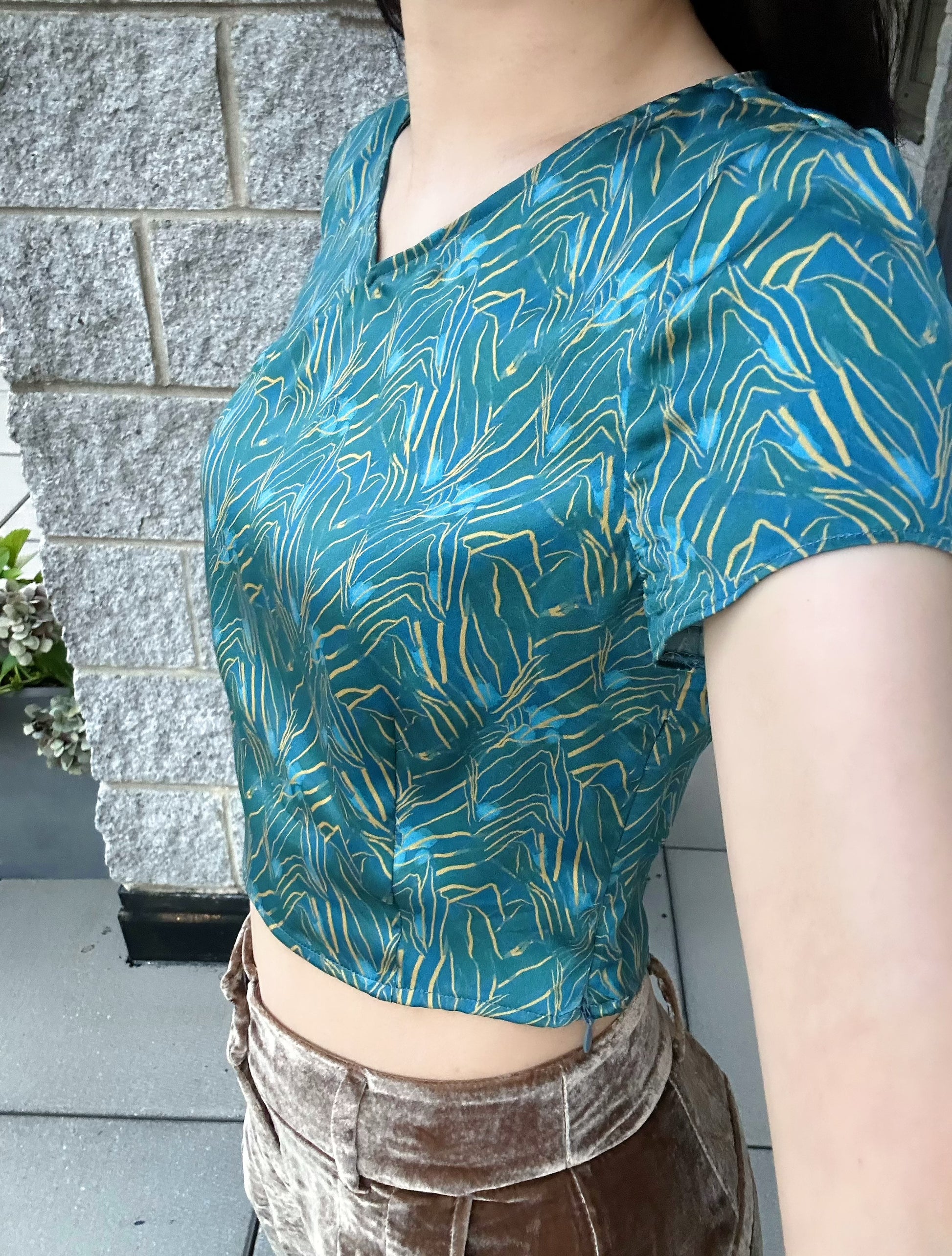 A woman wears the SPRING MOUNTAINS silk crop top and pairs it with brown velvet paints.  She exudes grace in this Modern Chinese chic style.