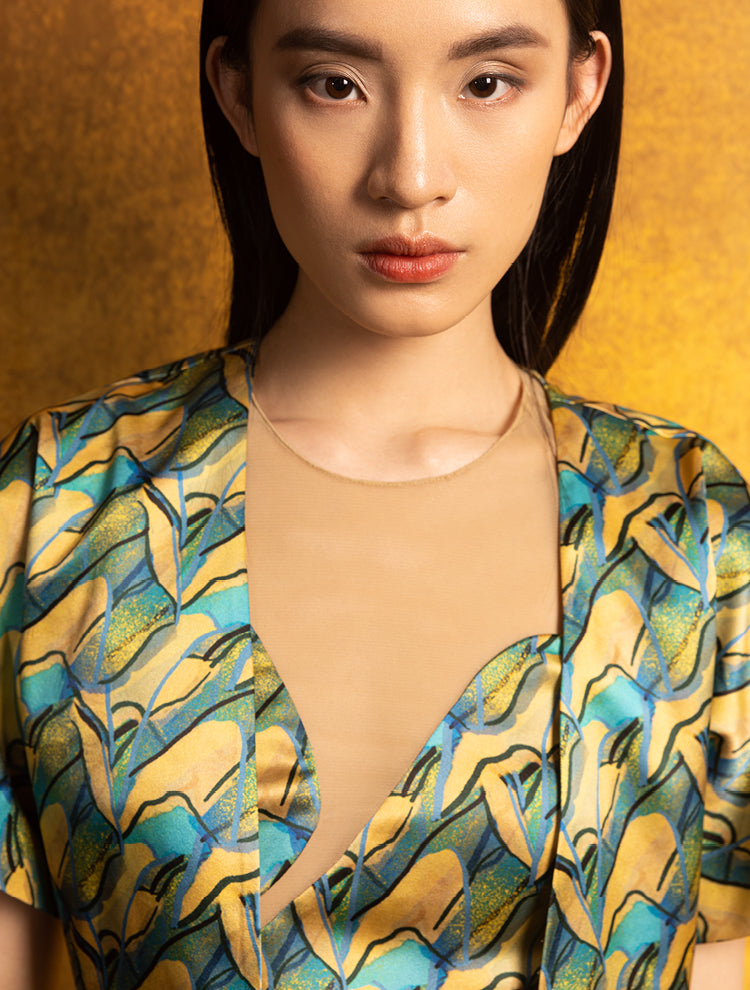 A woman wears a silk crop top and jacket. The set features the PANORAMA Print and is inspired by Chinese landscape paintings. She exudes grace in this Modern Chinese chic style. 